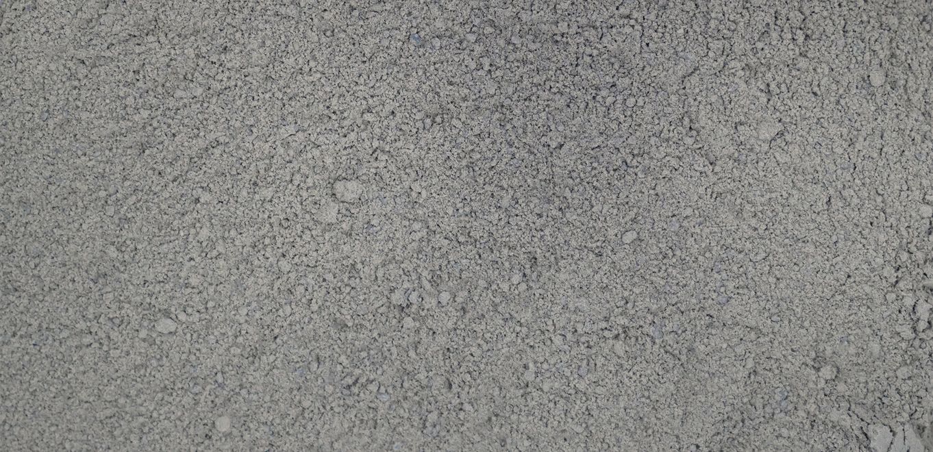 Image : poudre de roche finement broyée, gris foncé avec grains plus grossiers épars, le tout étalé sur une surface plane.