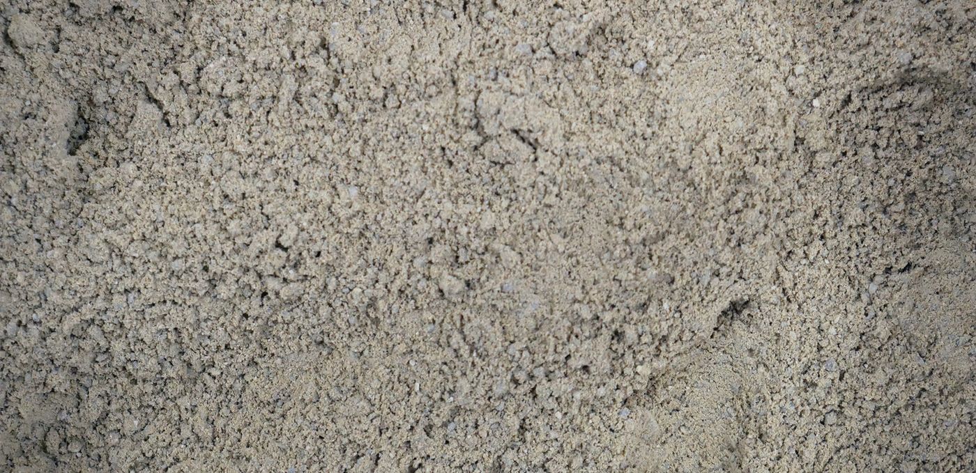 Image : poudre de roche finement broyée, de couleur gris-verdâtre foncé, avec grains plus grossiers épars, le tout étalé sur une surface plane.