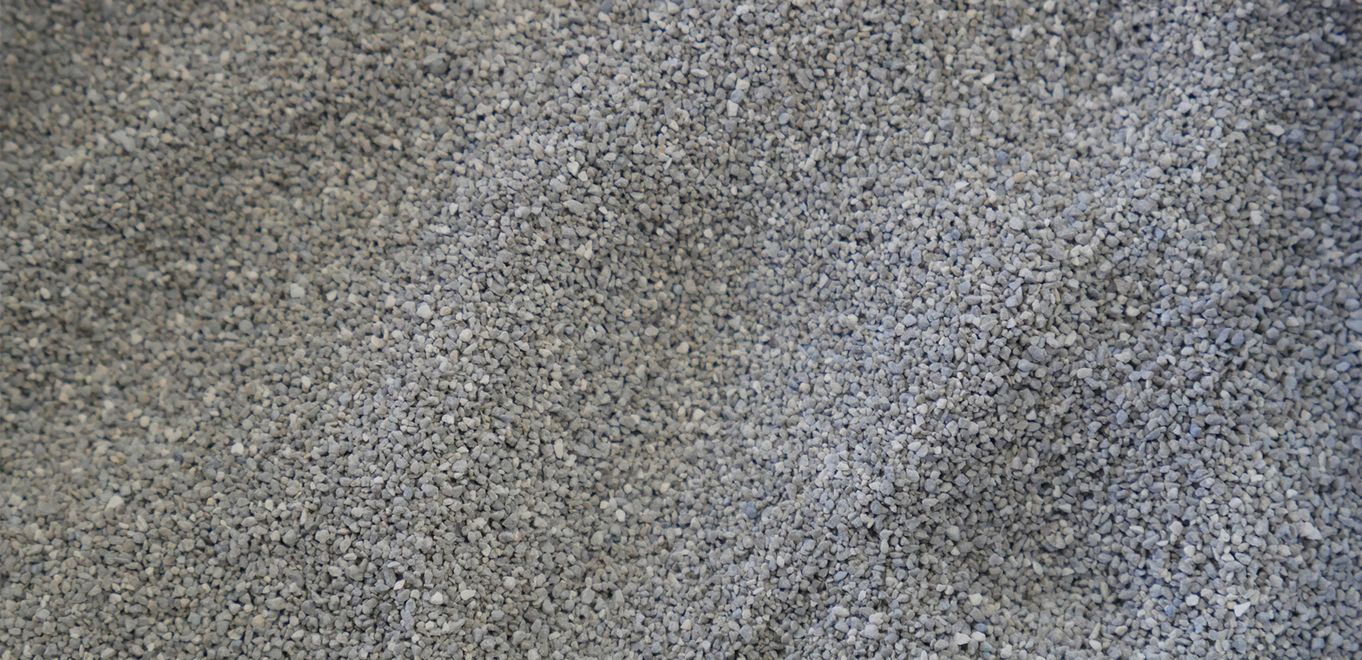 Image : poudre de roche grossièrement granulée, gris moyen et étalée sur une surface plane