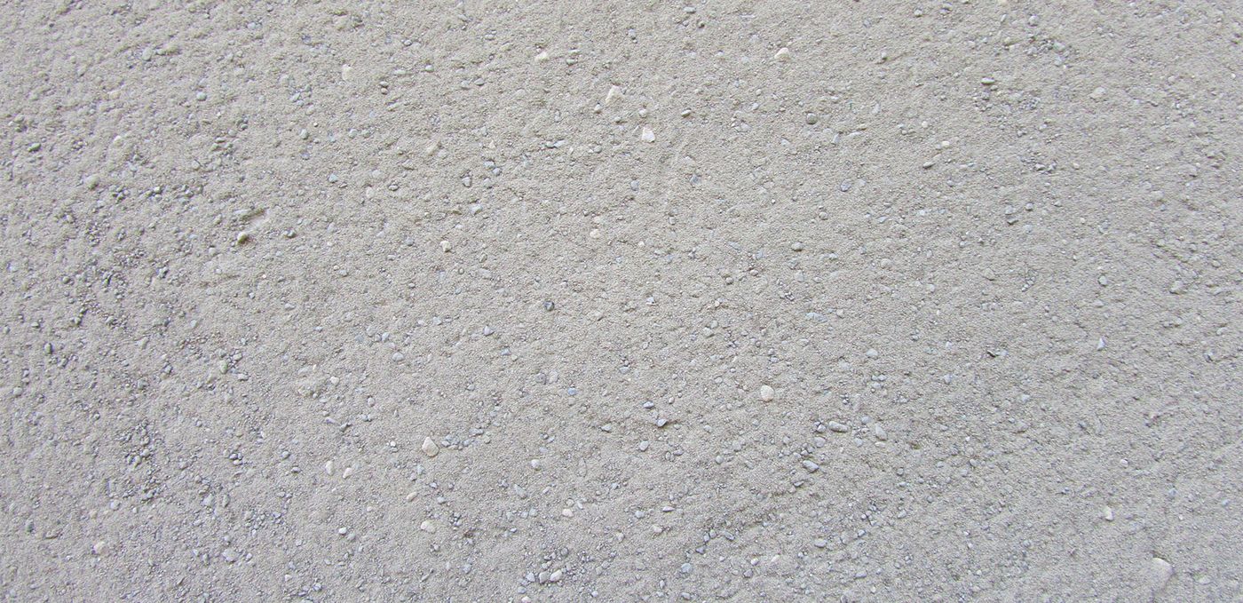Image : poudre de roche finement broyée, gris clair avec grains plus grossiers épars, le tout étalé sur une surface plane.